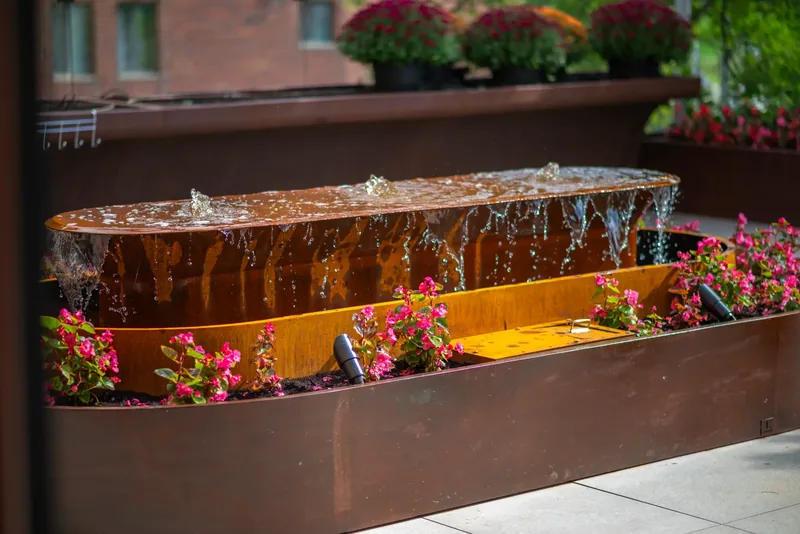 Steel water feature surrounded by flowers on the terrace