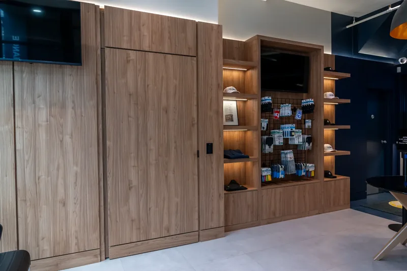 Floor-to-ceiling wood panelling with a flush door and illuminated merchandise shelving