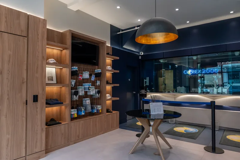 Illuminated wood shelving with travel accessories facing the navy teller area and a round glass table