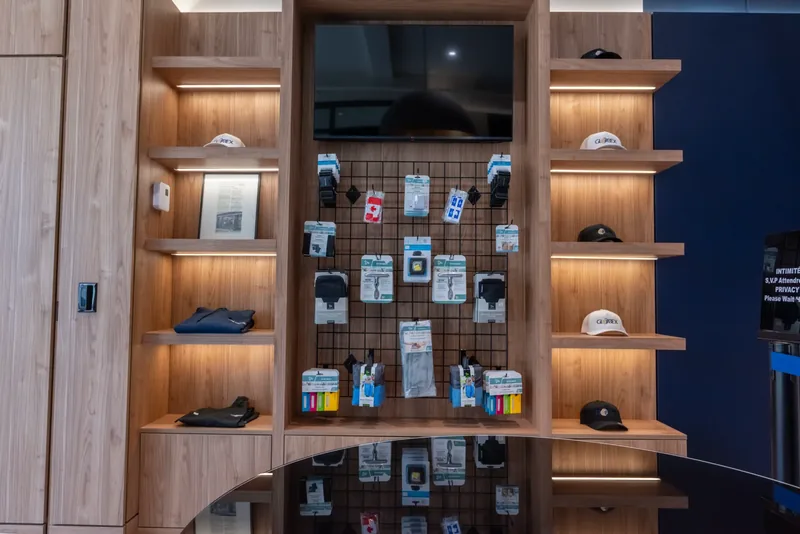 Merchandise wall with a central pegboard, a wall-mounted screen, and lit wood shelves on both sides