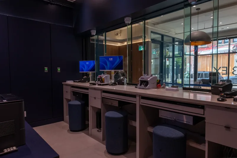 Teller stations behind the glass enclosure, with built-in counters, stools, and service equipment
