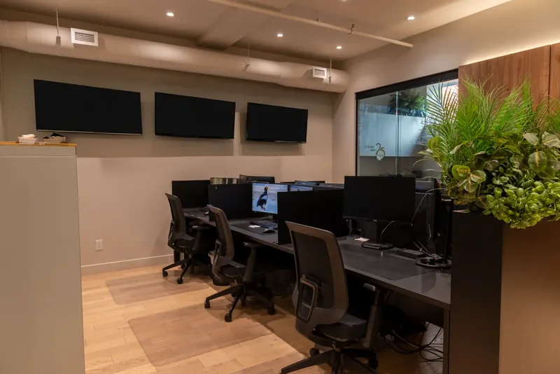Operations room with rows of workstations, wall-mounted screens, and a black planter of greenery