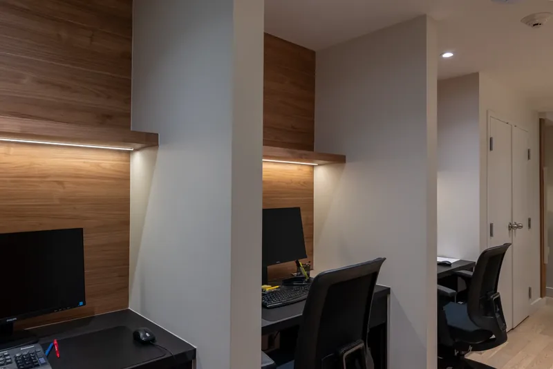 Desk nook with wood panelling and a lit shelf, beside a corridor of offices