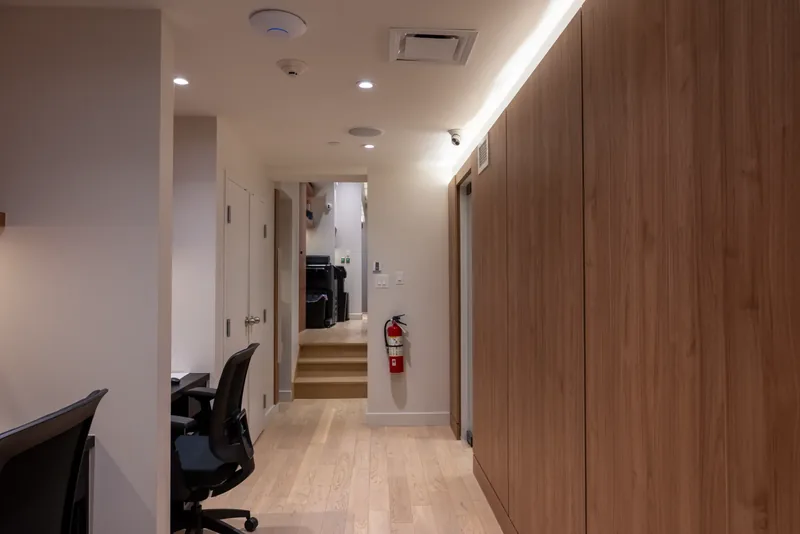 Office corridor with a tall wood-clad wall and cove lighting leading to the stairs