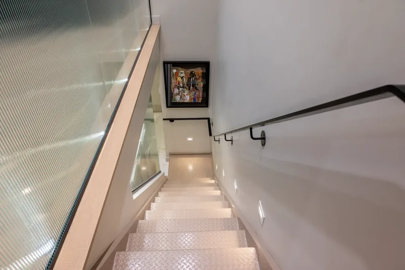 Staircase with a black handrail, a ribbed glass side, and framed artwork at the landing
