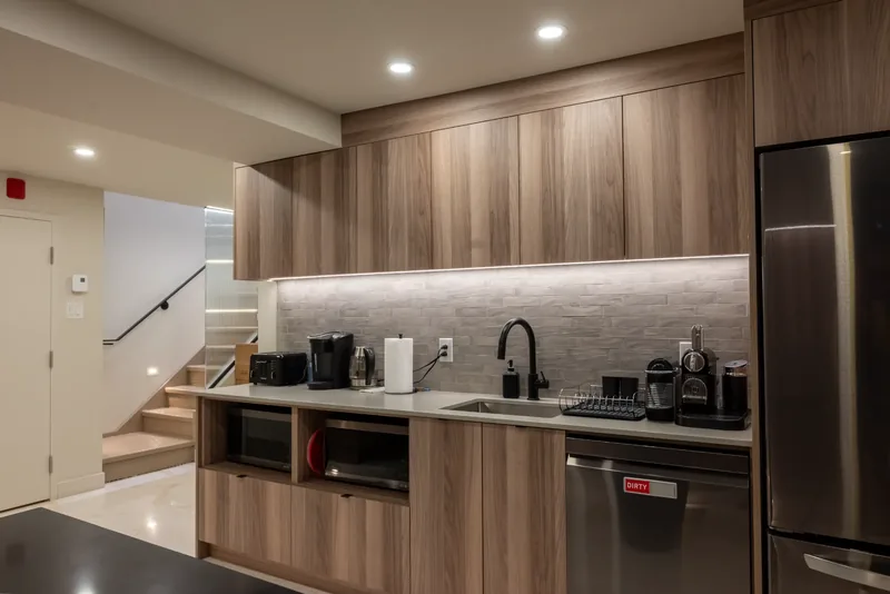 Staff kitchenette with wood cabinetry, a stone-look backsplash, and a stainless steel refrigerator