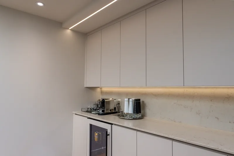 Coffee station with white flat-panel cabinetry, a stone counter, and under-cabinet lighting