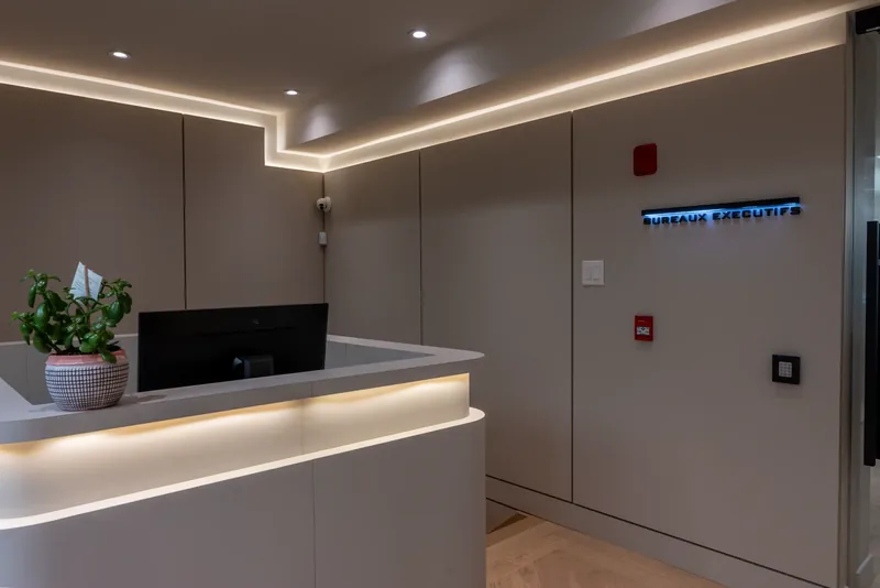 Curved reception desk with LED underlighting beneath a stepped, cove-lit ceiling