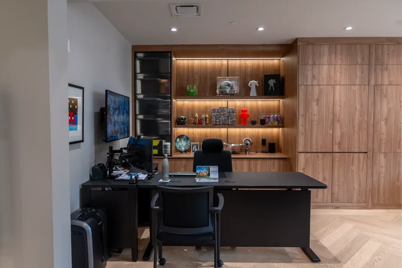 Executive desk facing a wall of wood millwork with illuminated shelves and collectibles