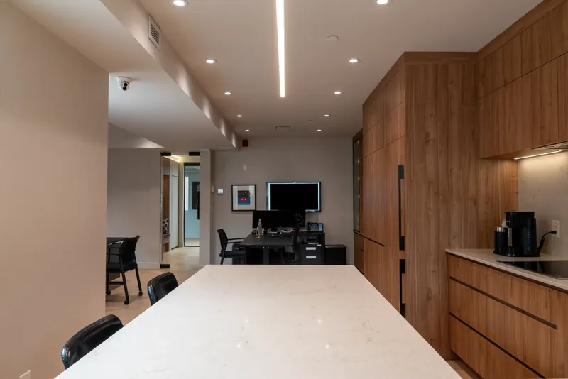 Large white stone kitchen island with wood cabinetry and an open view to the offices