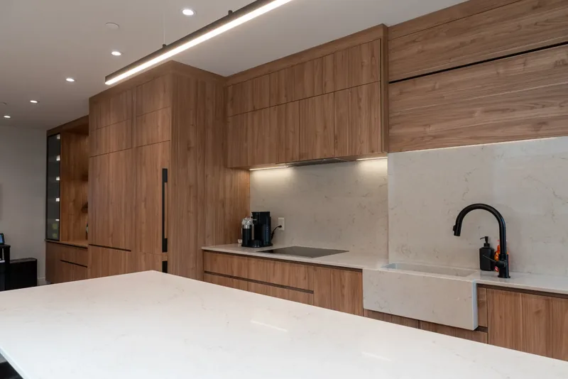 Wood kitchen cabinetry with a farmhouse sink, a black faucet, and a stone backsplash