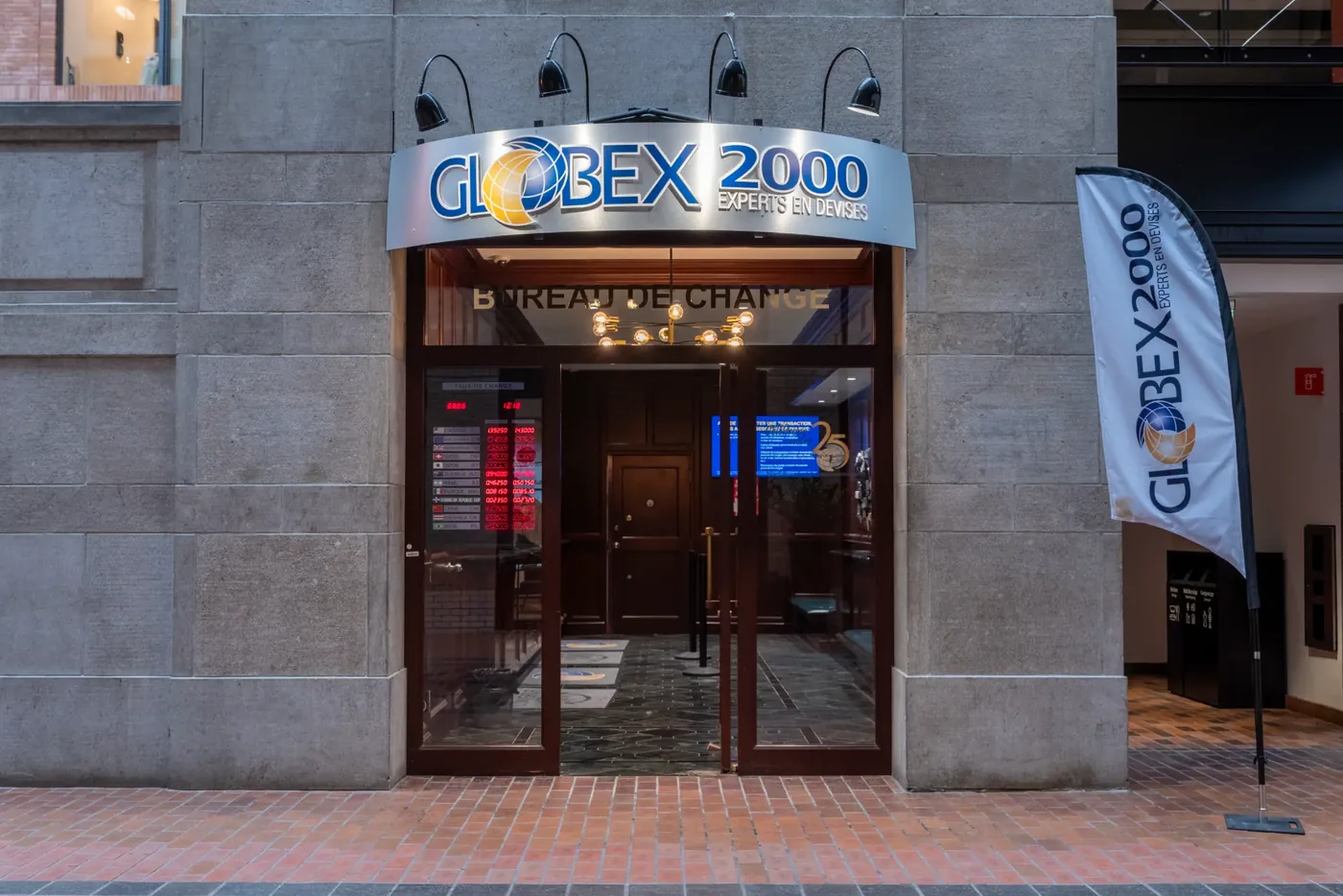 Globex 2000 storefront with a curved brushed-metal sign, black gooseneck lamps, and glass double doors framed in dark wood