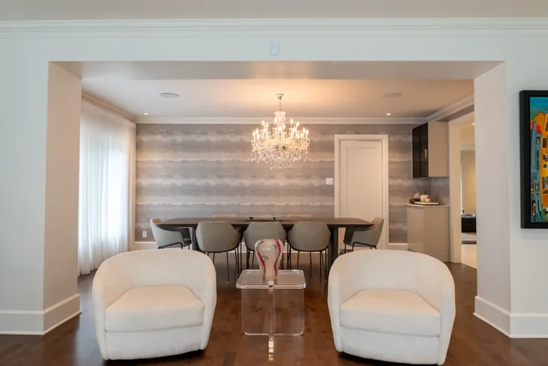Open living and dining area with white swivel lounge chairs and a crystal chandelier