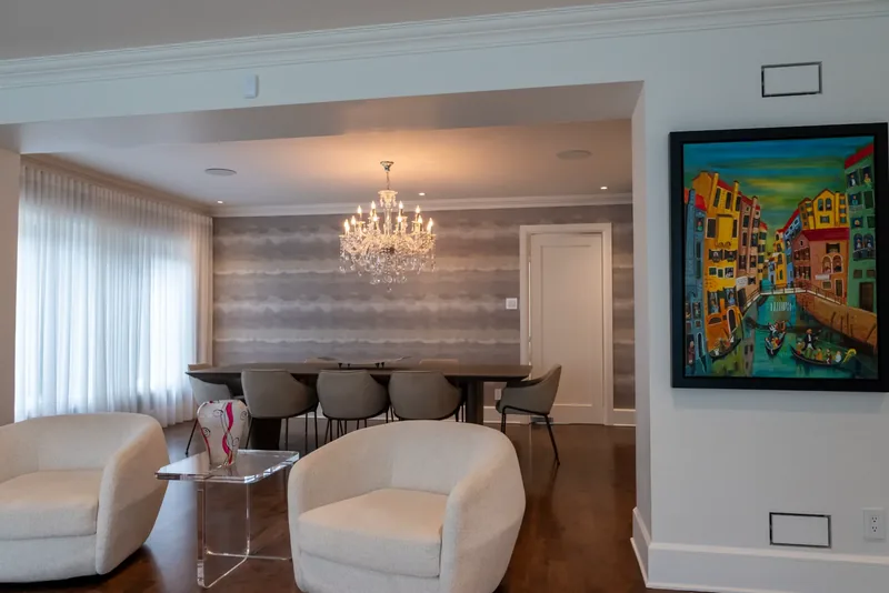 Open living and dining area with white swivel lounge chairs and a crystal chandelier