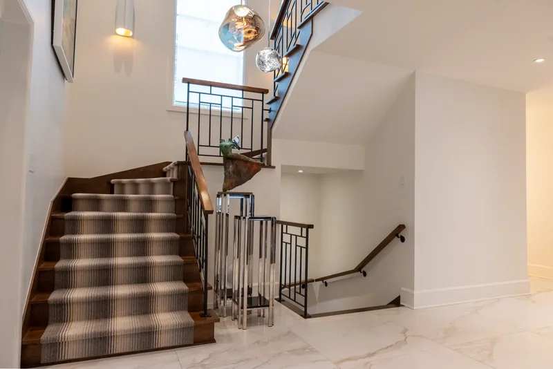 Open staircase with wood treads, a striped runner, and a black metal balustrade