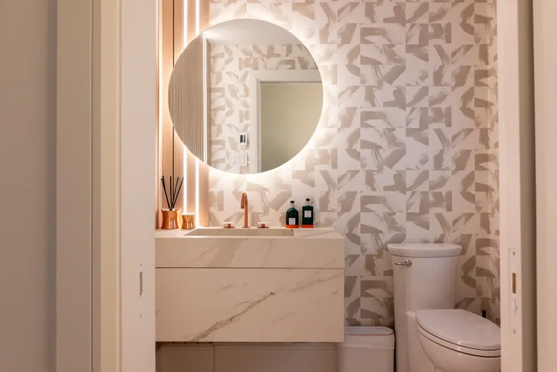 Powder room with a backlit round mirror, fluted wood panels, and a copper faucet