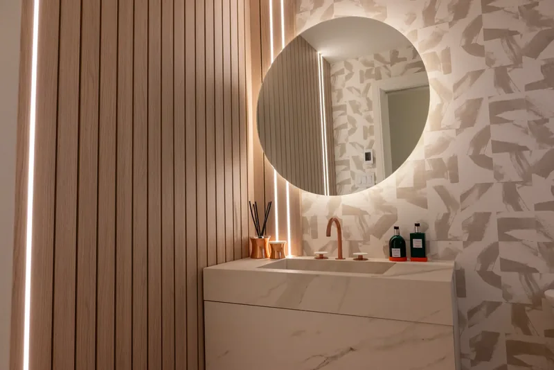 Powder room with a backlit round mirror, fluted wood panels, and a copper faucet