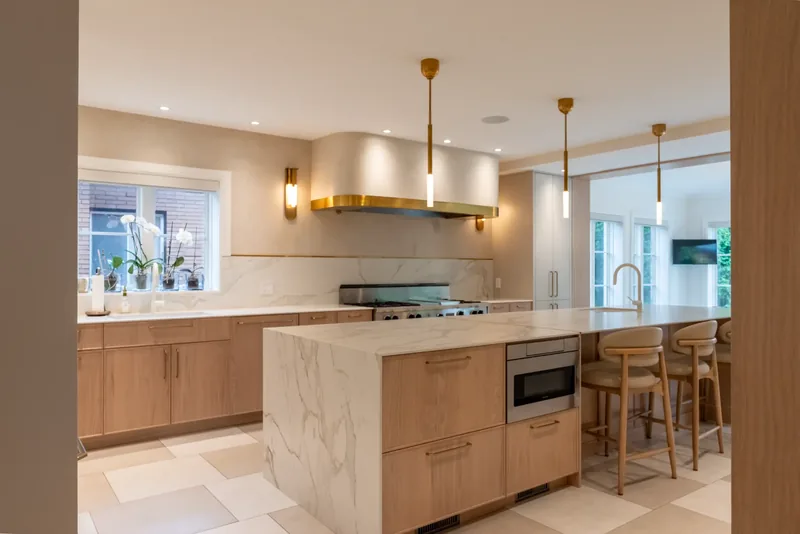 Kitchen with oak cabinetry, a marble-look waterfall island, and brass and glass pendants