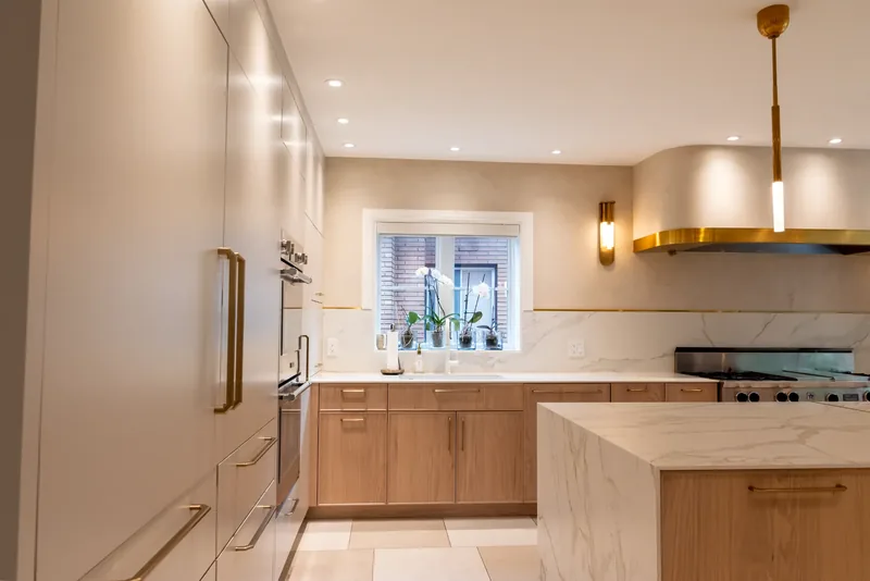 Kitchen with oak cabinetry, a marble-look waterfall island, and brass and glass pendants