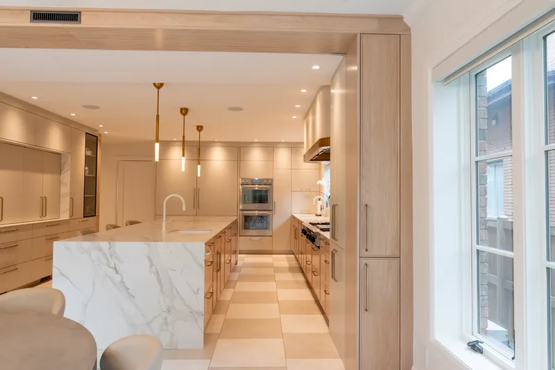 Kitchen with oak cabinetry, a marble-look waterfall island, and brass and glass pendants