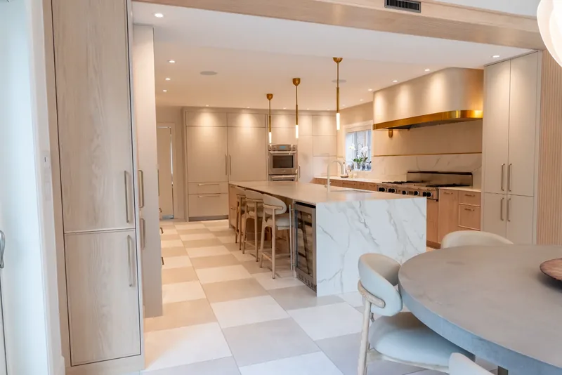 Kitchen with oak cabinetry, a marble-look waterfall island, and brass and glass pendants