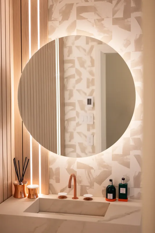 Powder room with a backlit round mirror, fluted wood panels, and a copper faucet