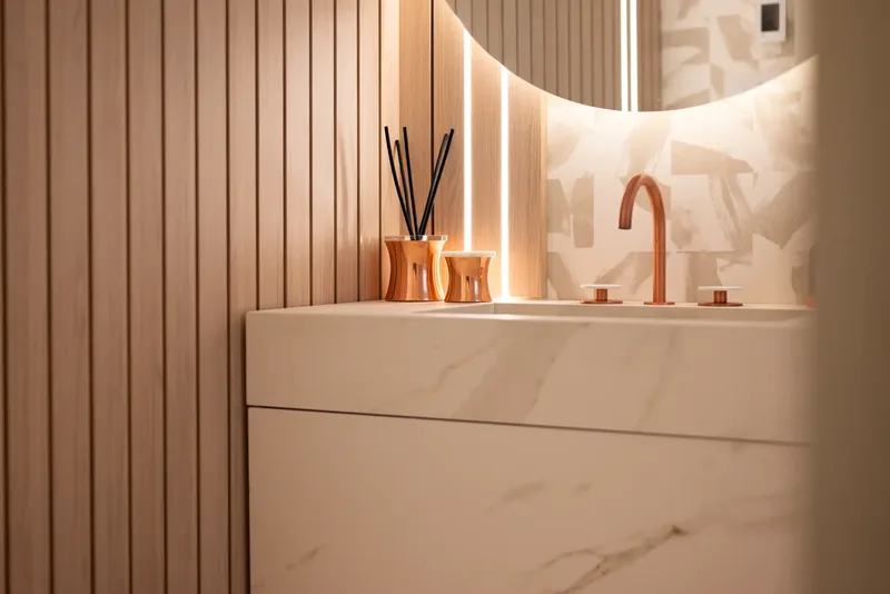 Powder room with a backlit round mirror, fluted wood panels, and a copper faucet