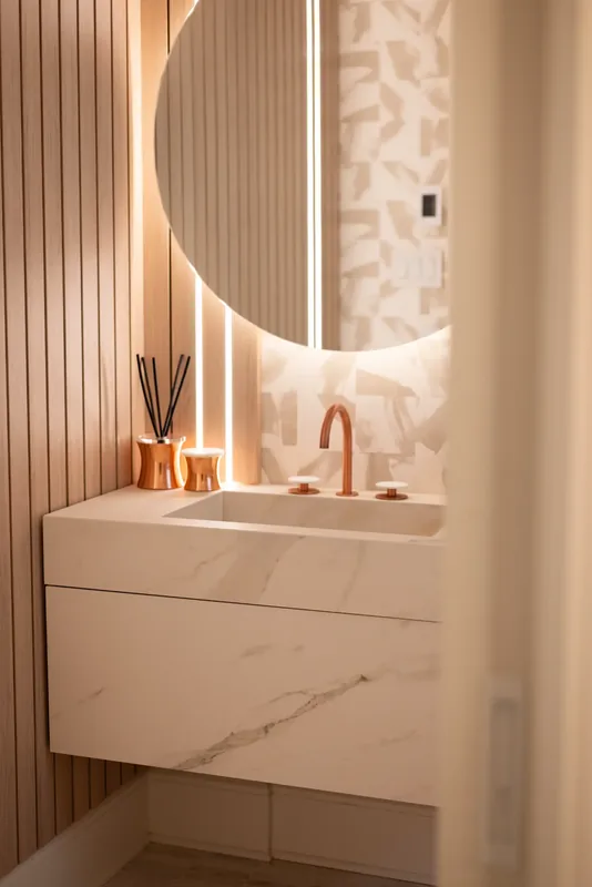 Powder room with a backlit round mirror, fluted wood panels, and a copper faucet
