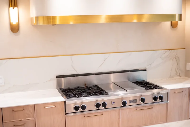 Professional range beneath a brass-banded hood and a marble-look backsplash