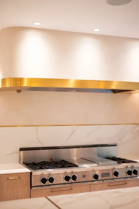 Professional range beneath a brass-banded hood and a marble-look backsplash