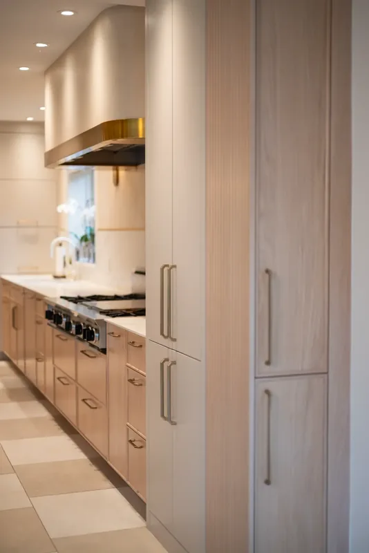 Kitchen with oak cabinetry, a marble-look waterfall island, and brass and glass pendants