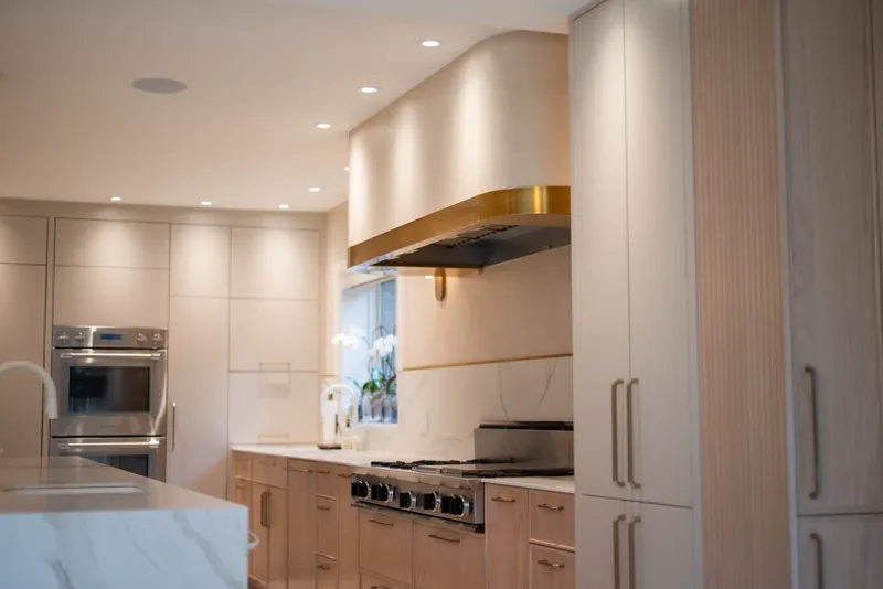 Kitchen with oak cabinetry, a marble-look waterfall island, and brass and glass pendants