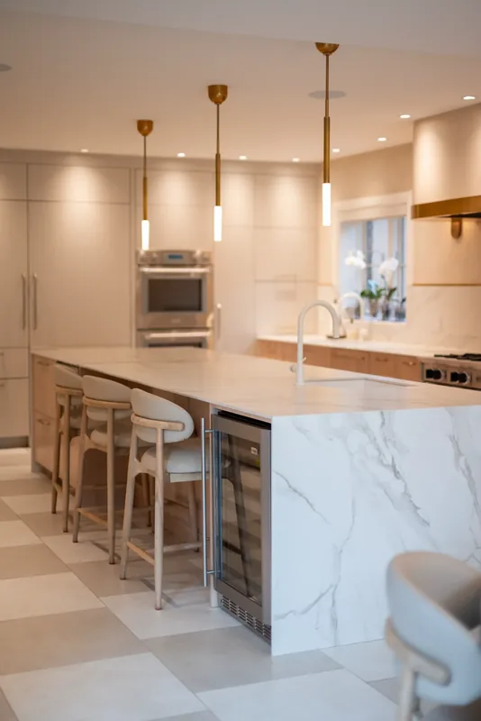 Kitchen with oak cabinetry, a marble-look waterfall island, and brass and glass pendants