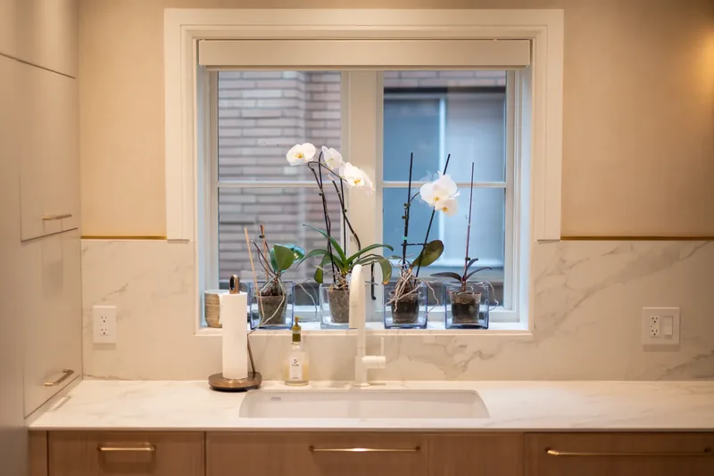Kitchen window counter with orchids and a marble-look backsplash