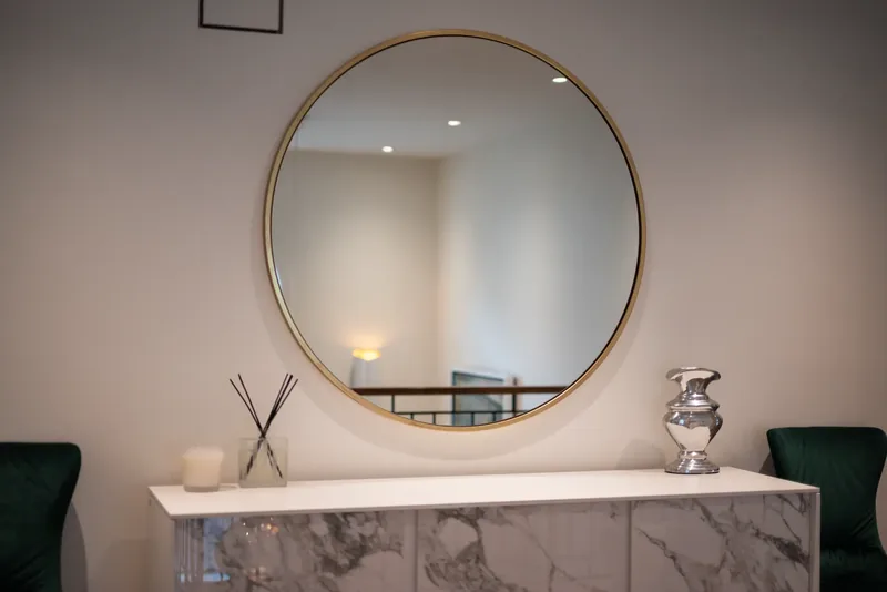 Landing with a round brass mirror, a marble-look console, and green velvet chairs