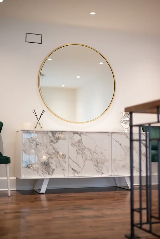 Landing with a round brass mirror, a marble-look console, and green velvet chairs