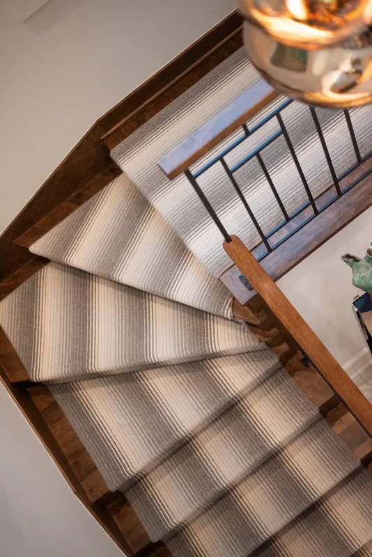 View from above of the staircase, its wood treads, and striped runner