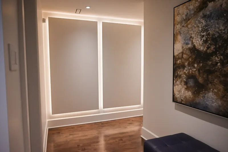 Backlit recessed wall panels, a large abstract artwork, and a tufted bench