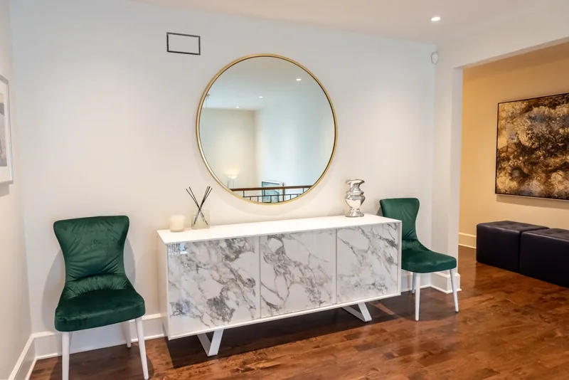 Landing with a round brass mirror, a marble-look console, and green velvet chairs