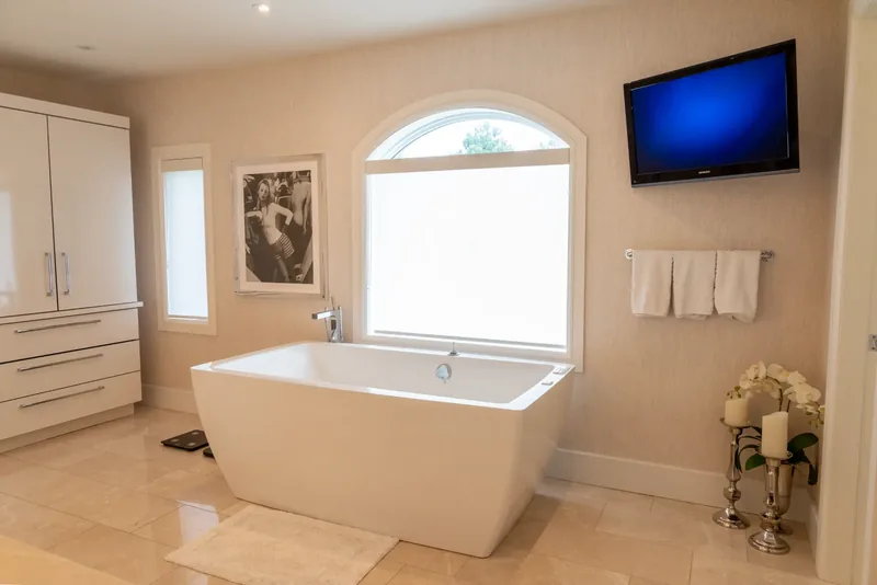 Freestanding soaking tub beneath an arched window in the primary ensuite