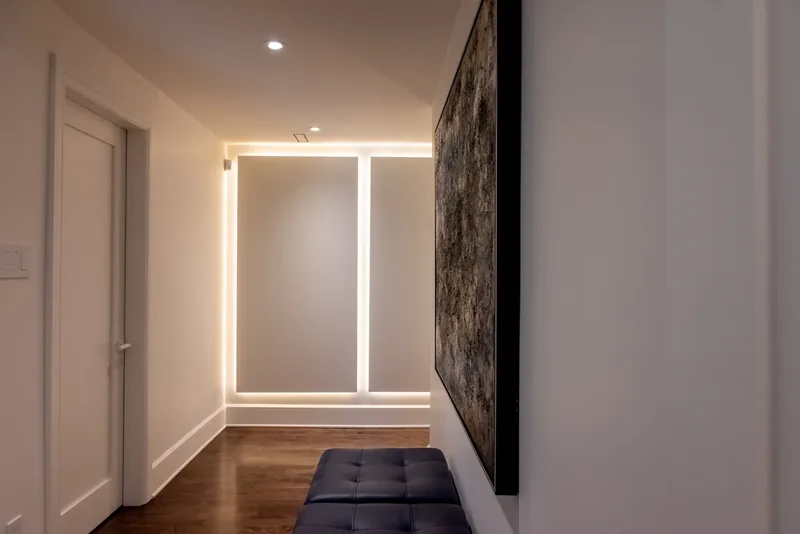 Backlit recessed wall panels, a large abstract artwork, and a tufted bench