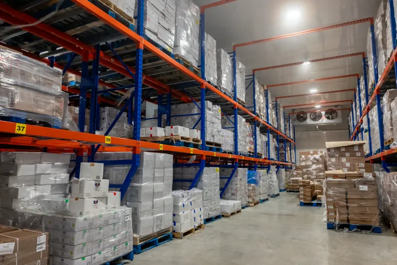 Travées de palettiers numérotées chargées de boîtes, avec évaporateurs au bout de l’allée