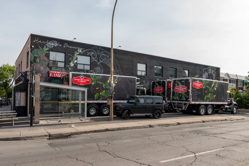 Dark brick Iasenza building with a large botanical mural and two branded delivery trucks parked along the street