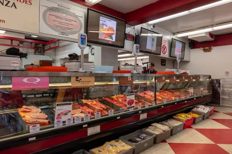 Long refrigerated meat counter with digital menu screens above and a butcher at work behind the display