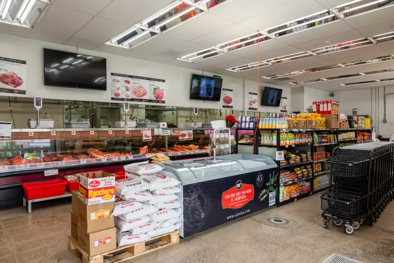 Bright, open store with a long butcher counter, overhead screens, a branded chest freezer, and shopping carts