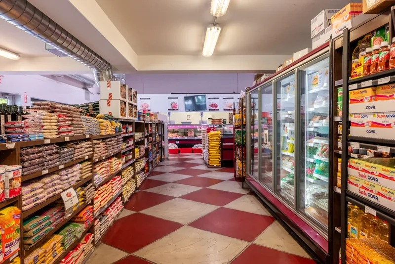 Long grocery aisle with stocked shelving on one side and glass-door freezers on the other, over a checkered floor