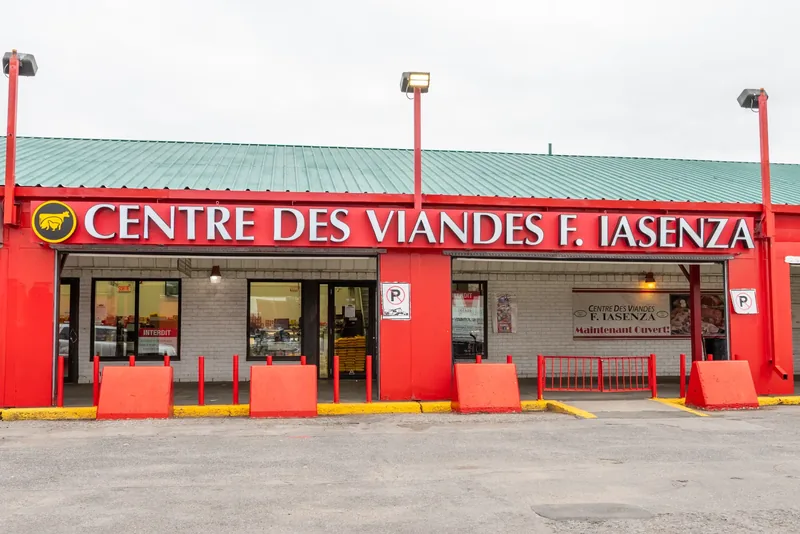Single-storey Iasenza store with a red facade, a large illuminated sign, a green metal roof, red bollards, and a parking lot