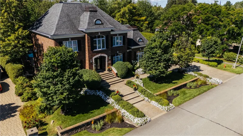 Front of the brick residence with stone steps, clipped boxwood, and flower beds