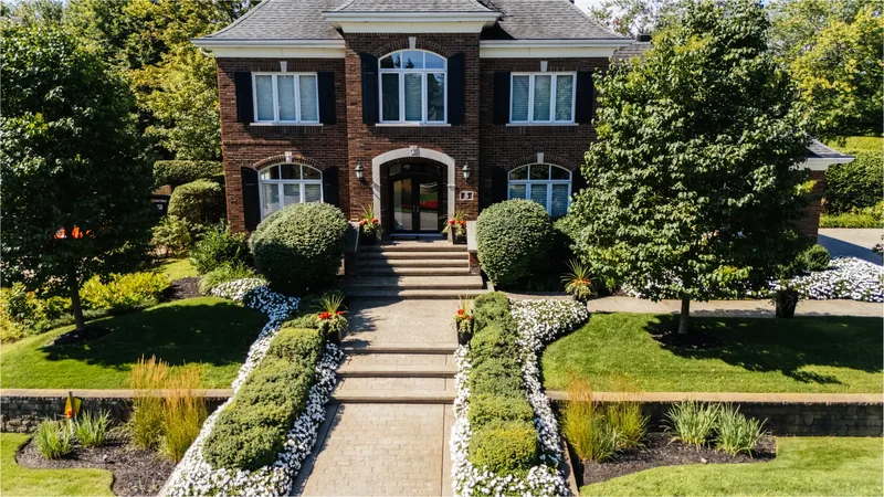 Front of the brick residence with stone steps, clipped boxwood, and flower beds