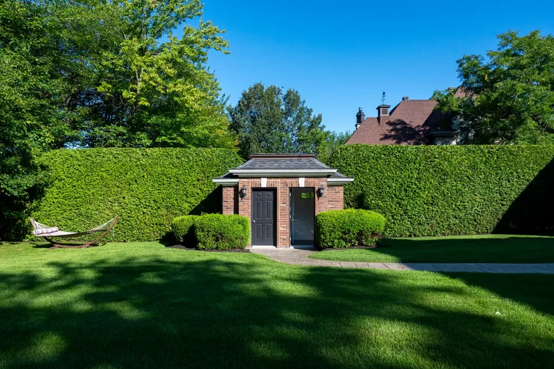 Brick garden pavilion framed by tall cedar hedges